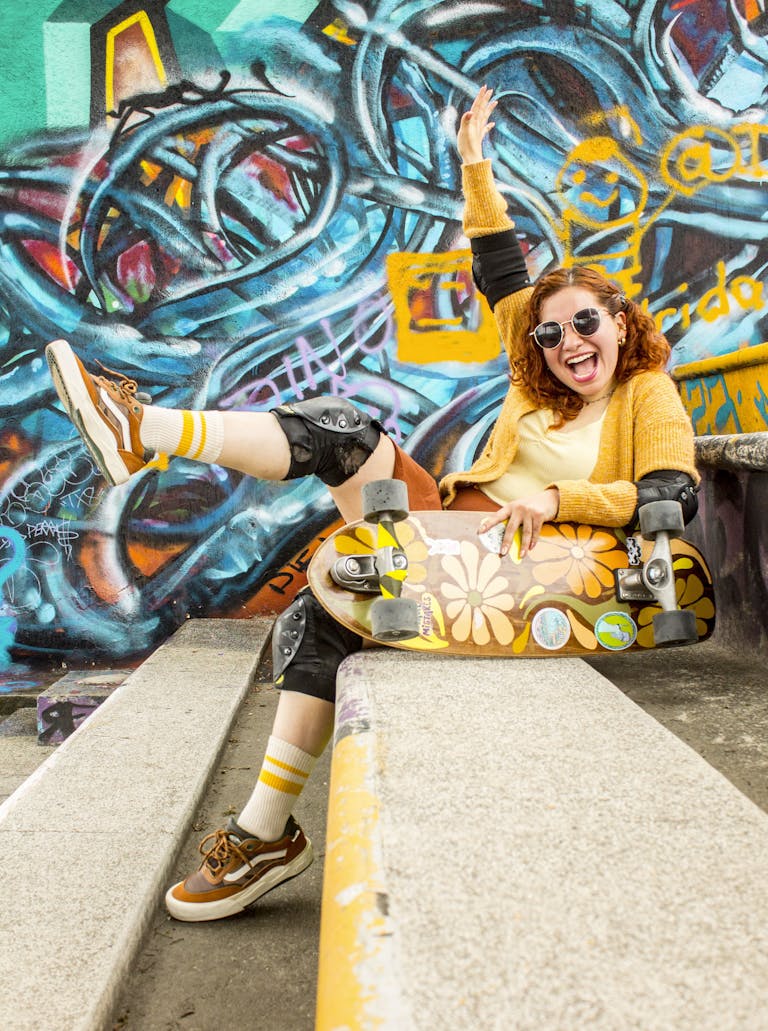 Cheerful young woman with skateboard posing against vibrant graffiti wall.