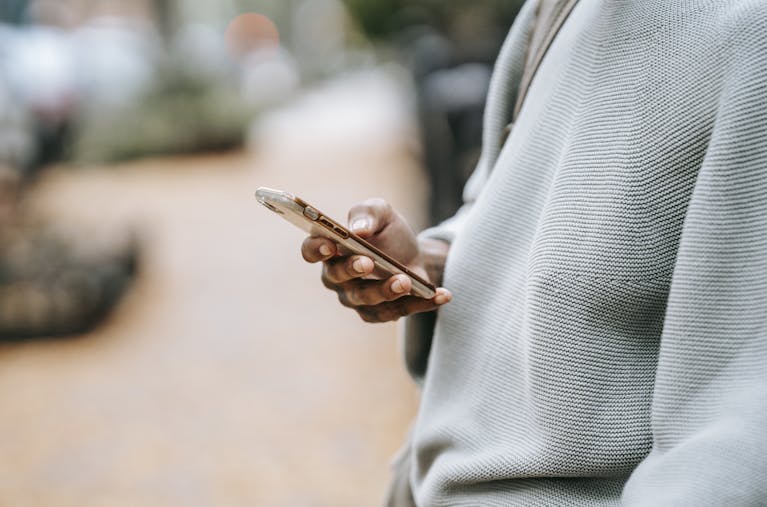 A person casually uses a smartphone outdoors in an urban environment, focusing on connection.